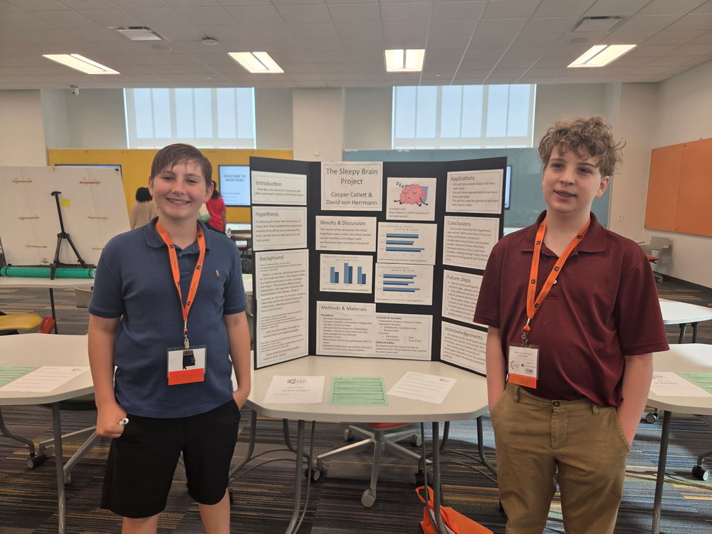 Cooper and David standing in front of their science fair poster board