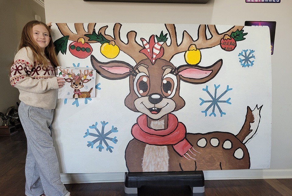 Fourth grader Charlotte LeVere stands beside her artwork of a reindeer. 