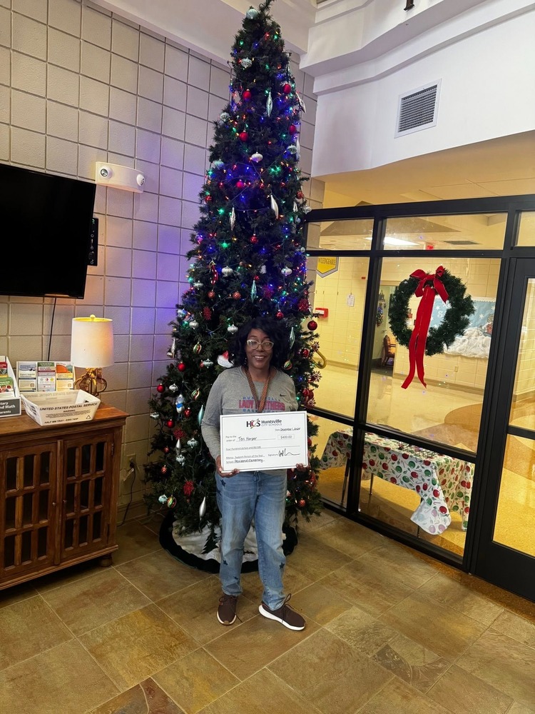 Teri Harper standing outside the office area holding a HCS check for Support Staff of the Year