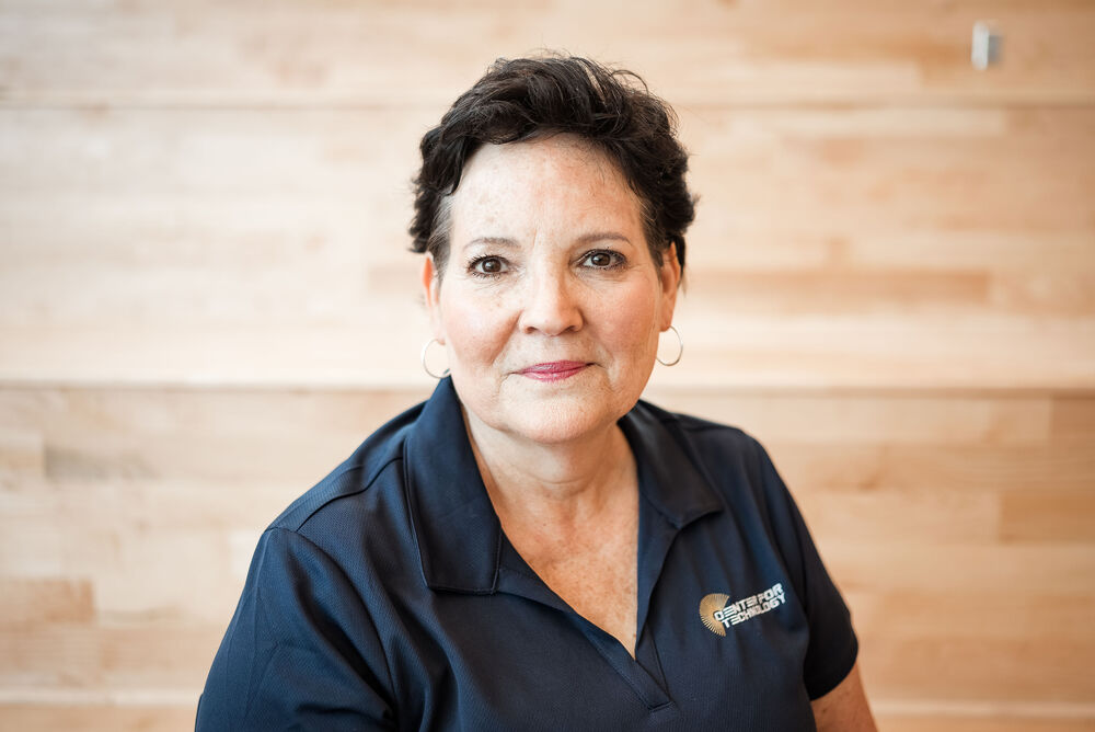 Karen Rodriguez, Culinary Teacher wearing a navy blue Center for Technology polo in front of the stairs.