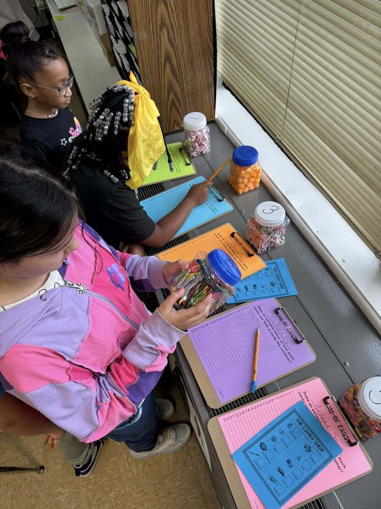 Two young girls are looking at jars of candy with estimation papers in front of them.
