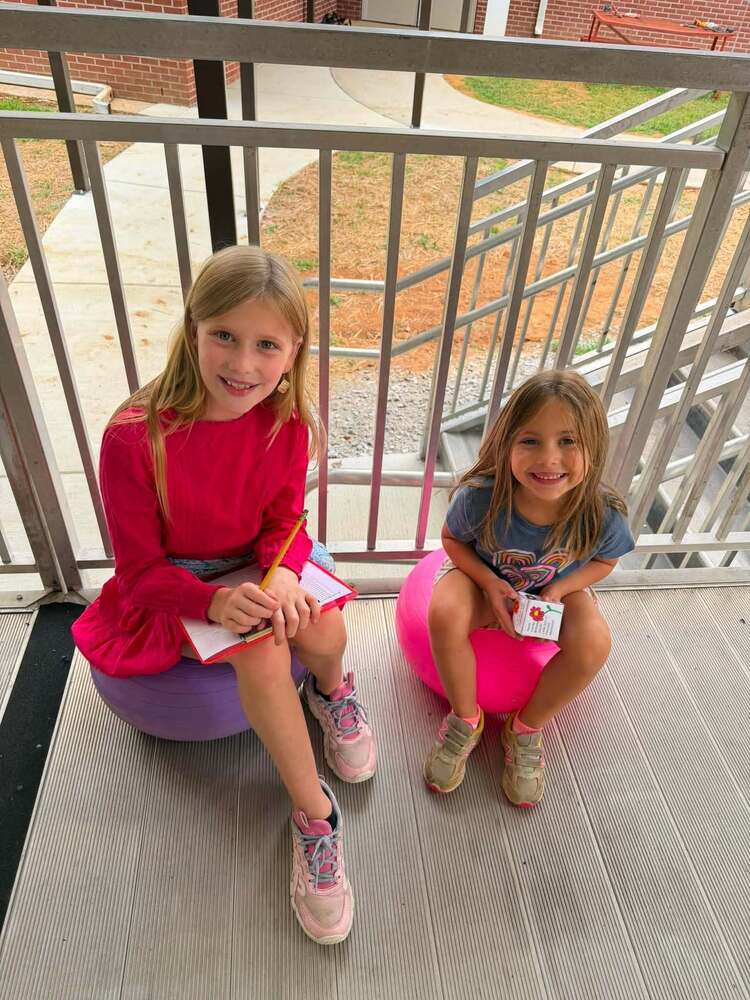 two students sitting outside one holding clipboard and other holding paper cube