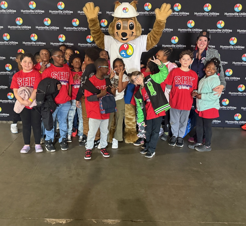Reddy Kilowatt standing with Mrs. Matthew's 4th grade class in front of a Huntsville Utilities back drop