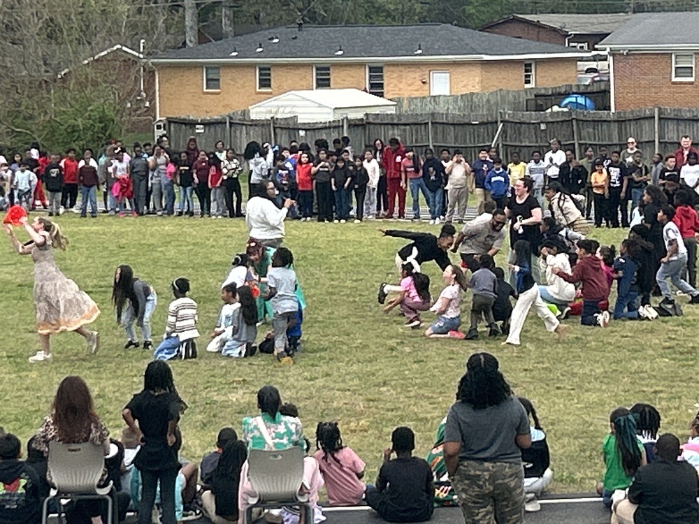 Children and staff participate in a lively outdoor pep rally on a grassy field