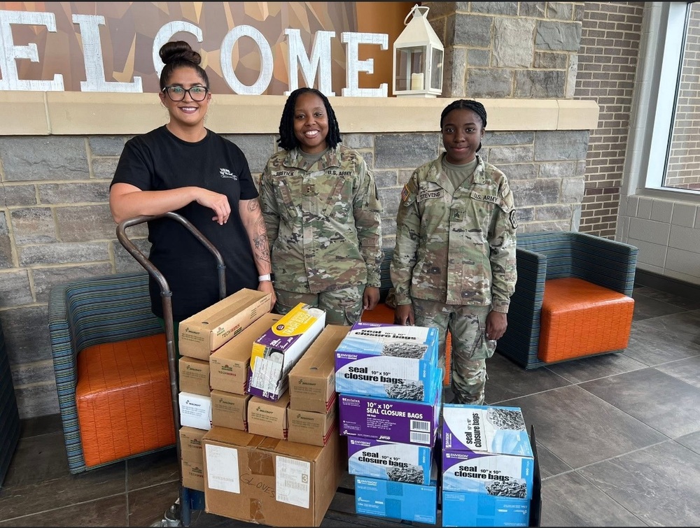 1 woman and 2 women soldiers standing in a school lobby with supplies