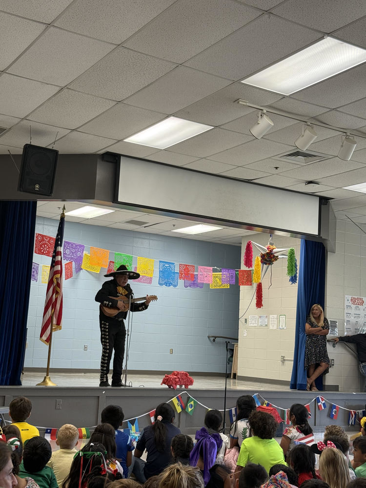Mariachi performer on stage in the Chaffee cafeteria that is decorated for Hispanic Heritage Month. Below him is students watching as he performs 