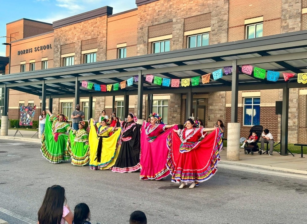 Women dressed in cultural dresses posing in front of the school for the Hispanic Heritage Festival