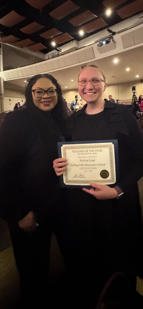 Mrs. Agun and Mrs Loar smile while Mrs. Loar holds a Teacher of the Year certificate for Rolling Hills Elementary School.