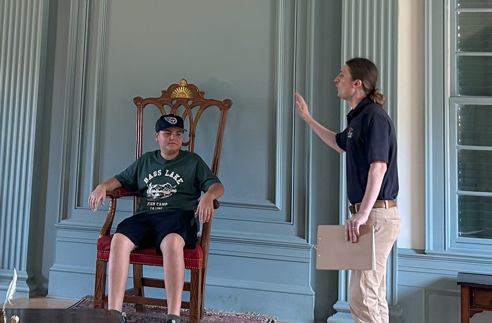 Young male student sits on a chair as an adult male actor interviews him. 