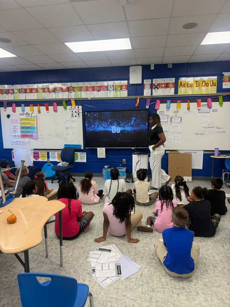 A teacher at the smartboard screen teaching students sitting and watching