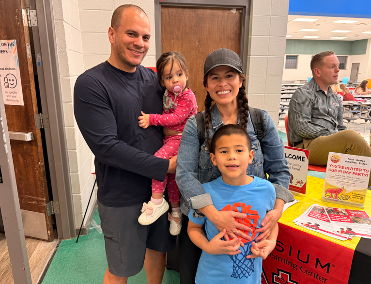 Father and mother with their son and daughter standing in front of the Mathnasium table