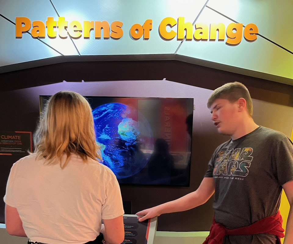 Female student and male student look at a science exhibit on climate.
