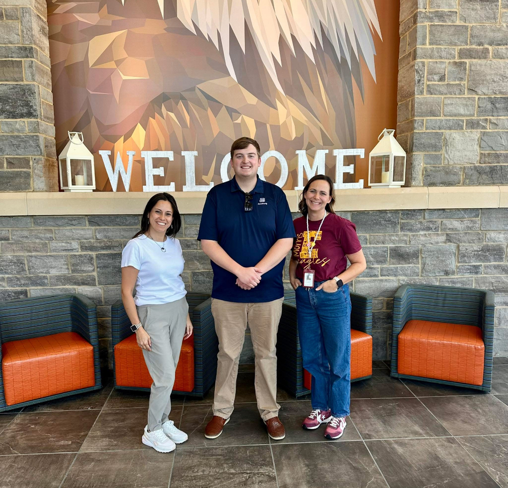 two women and a man standing in the middle of them posing in a school lobby