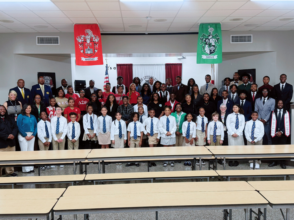 Several men, women, and children standing in front of the stage in the lunchroom