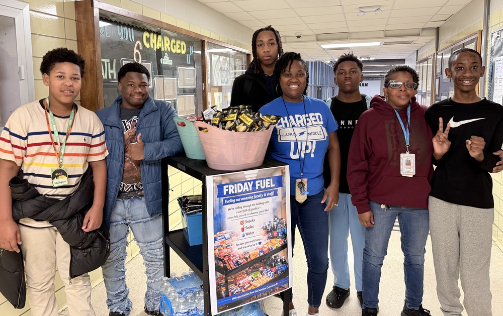 Chapman Middle School students, Ms. Cowans, and Mrs. Smith pose in a hallway next to a "Friday Fuel" snack cart filled with chips and water.