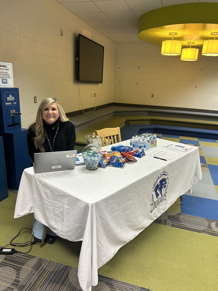 Mrs. Atchely sits at a table awaiting parents