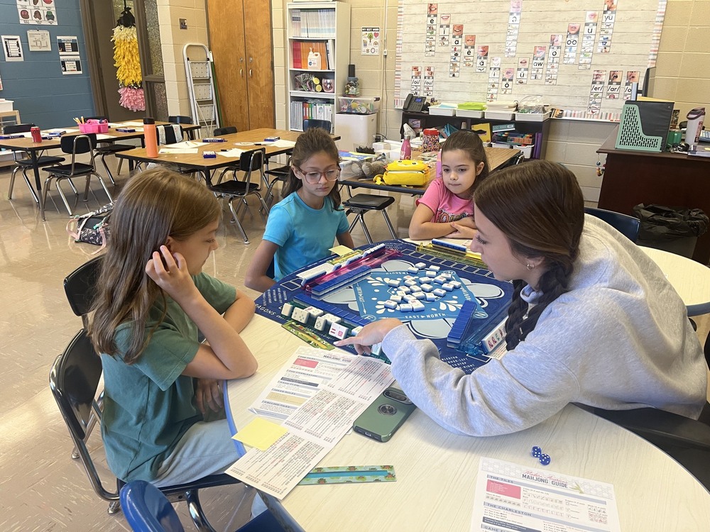 Three young female students are being directed by their teacher, Chrissy Gleason, on the game of Mahjong.