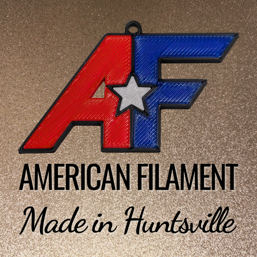 A 3D-printed red, white, and blue logo with the letters “AF” and a star in the center. Below the logo, the text reads “American Filament” and “Made in Huntsville” on a gold textured background.
