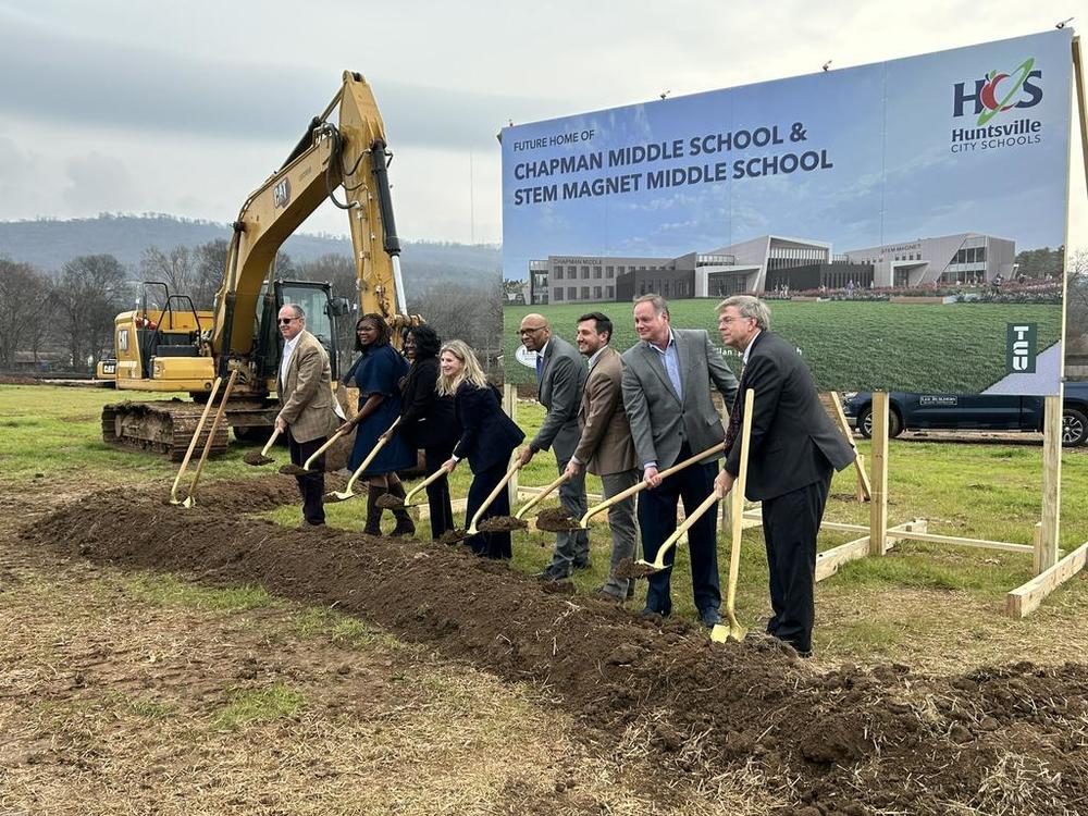 District and City officials shovel dirt in front of a large image of the artist's rendering at the Chapman and STEM facility groundbreaking
