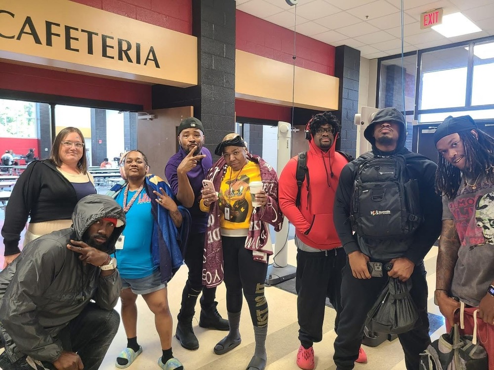 Teachers and principals standing in front of the cafeteria dress up like students posing for picture