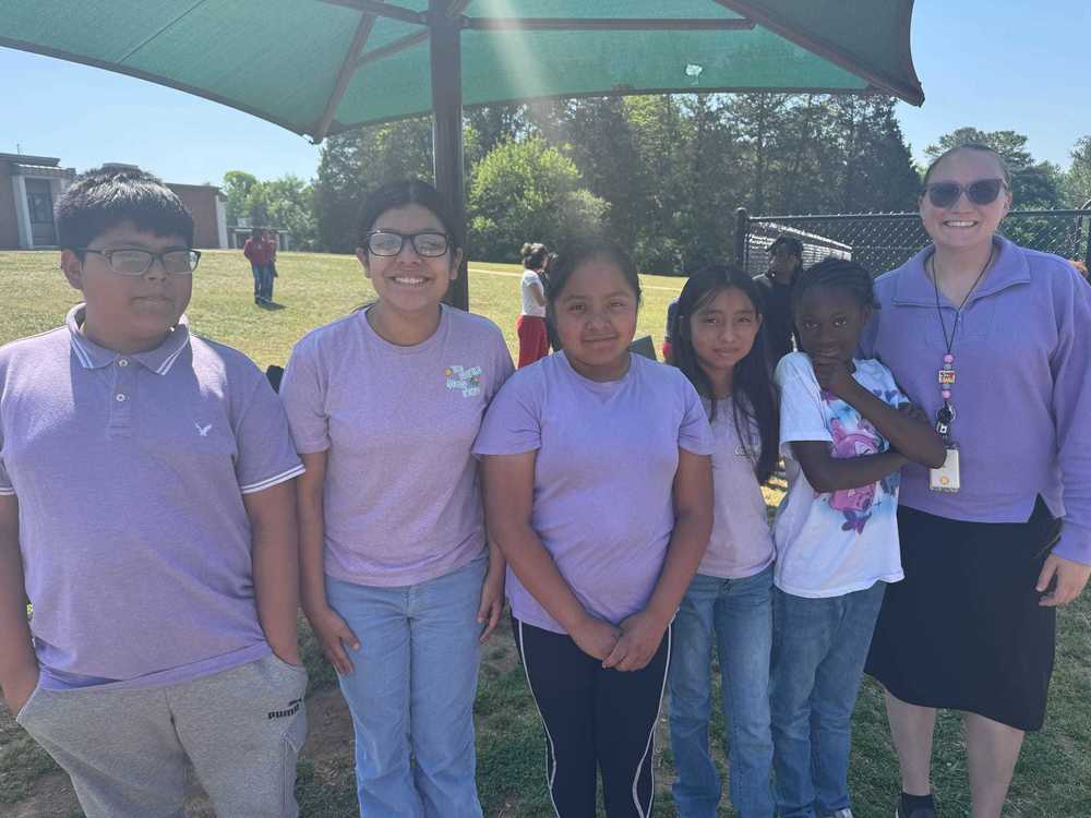 A teacher and five students stand outside smiling showing their purple clothing