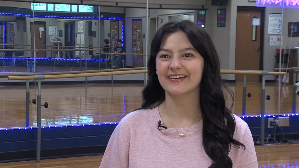 Erin Duus, a senior at Lee High School, stands in the school’s dance studio. She is smiling and speaking during an interview, with mirrored walls, blue LED lighting, and dance barres visible in the background.
