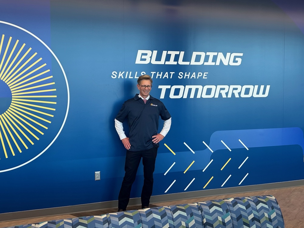 Dr. Mackey, State Superintendent of Alabama, posing in front of CTE wall that says Building Skills that Shape Tomorrow