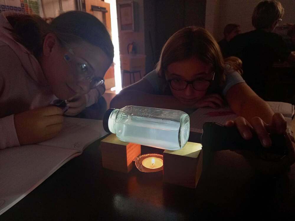 Image of two 6th grade girls in dark room looking at a jar with light shining through