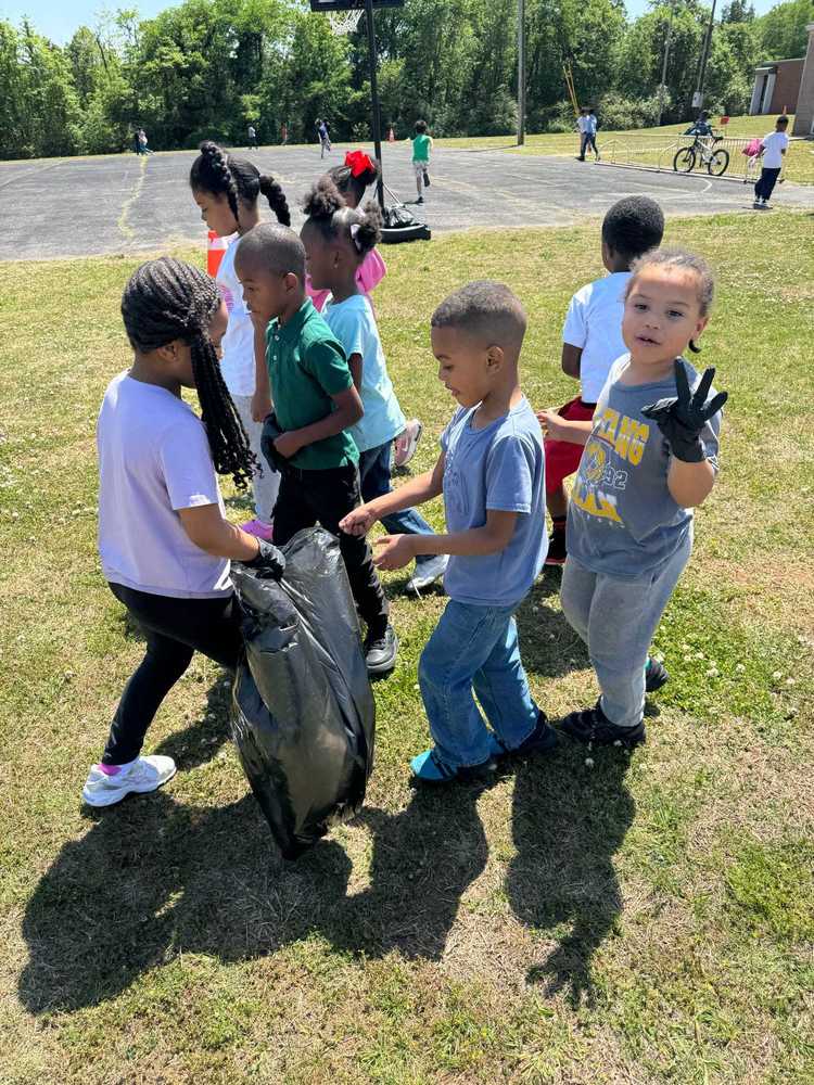 Young students warning gloves work together outside, picking up trash and holding a large garbage bag.