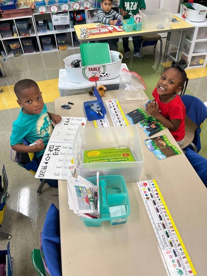 2 of Mrs.Neighbor's students at table during learning station working on math skills. Pictured on the table is center supplies 