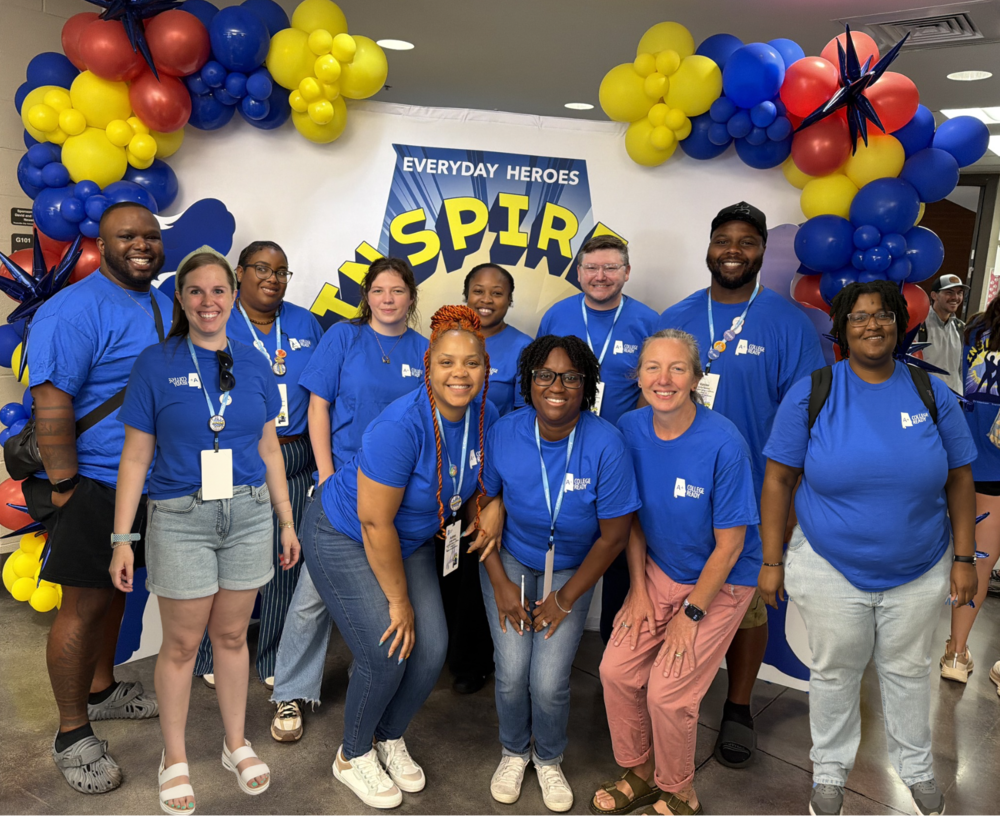 A group of ten Chapman Middle School teachers wearing matching blue "A+ College READY" t-shirts and lanyards smile together in front of a white photo backdrop featuring an arch of red, blue, and yellow balloons.