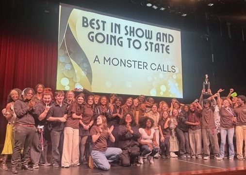 Lee High Performing Arts students from A Monster Calls stand on stage applauding after receiving their award for Best in Show at the District Trumbauer Festival. Behind them, a large screen displays the message “Best in Show and Going to State: A Monster Calls.”