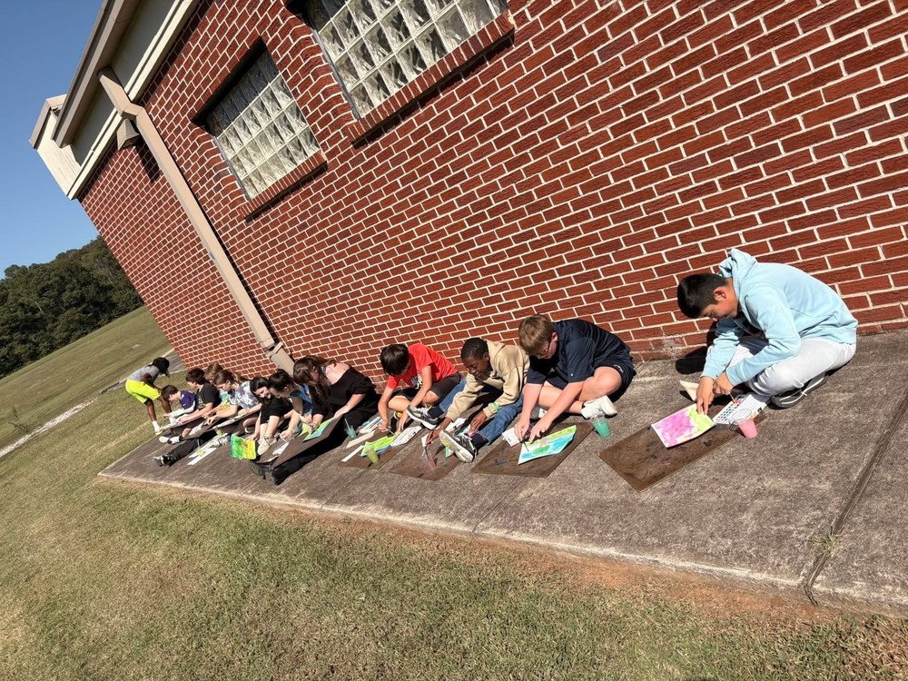 7th grade art students sitting on the ground against the wall painting