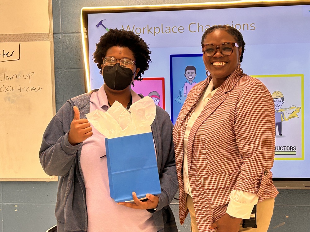 Ms. Jones and Mrs. Peavy post with a gift bag in front of the interactive board in Ms. Jones's classroom. 