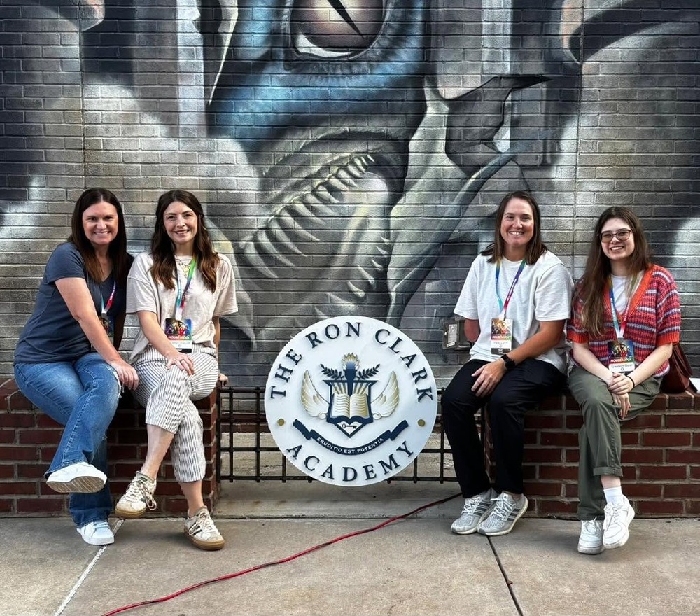 Mrs. Frazier, Mrs. Ratcliff, Ms. Lynch and Ms. Dean sit around a seal that says The Ron Clark Academy