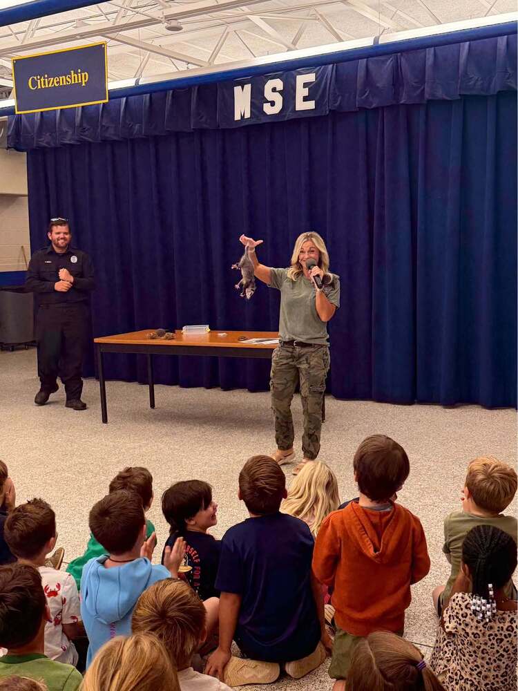 woman standing in front with opossum hanging upside down in front of students