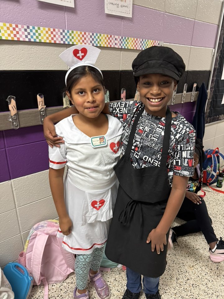 Two students are dressed up for their future careers. A girl dressed as a nurse is standing with a boy dressed as a chef.