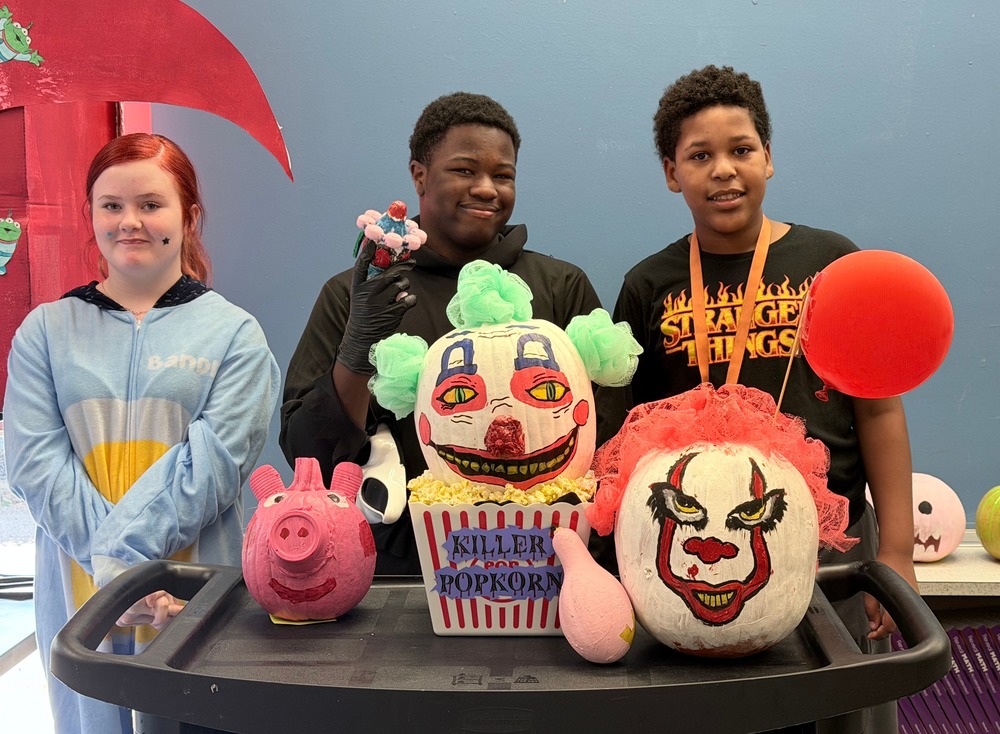 The three winners of the 2nd Annual SGA Pumpkin Contest are standing proudly behind their pumpkins in the library.