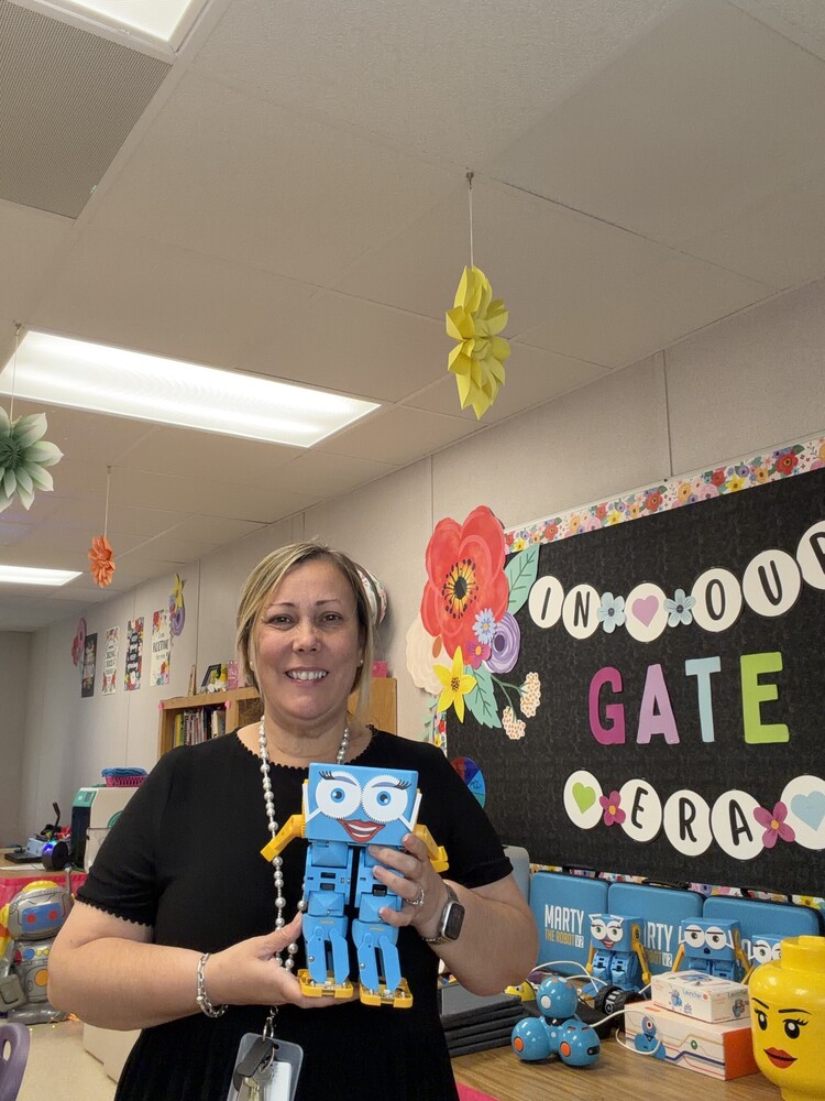 teacher holding a blue robot in hand inside classroom