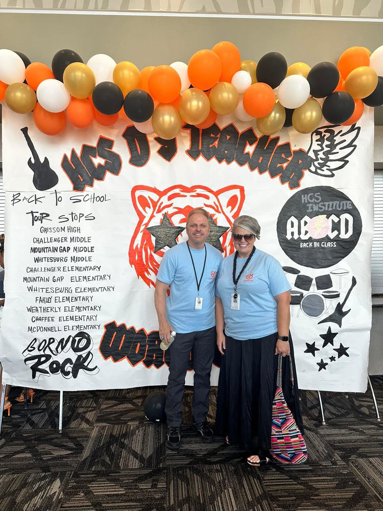 Tim Lanza and April Clark at Grissom High School in front of a rock banner. Tim and April are wearing blue Chaffee shirts!