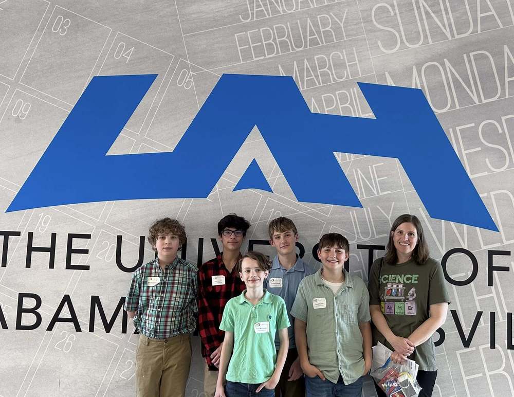 Students and Mrs. Heimbeck standing in front of a sign that says UAH at the Regional Science Fair