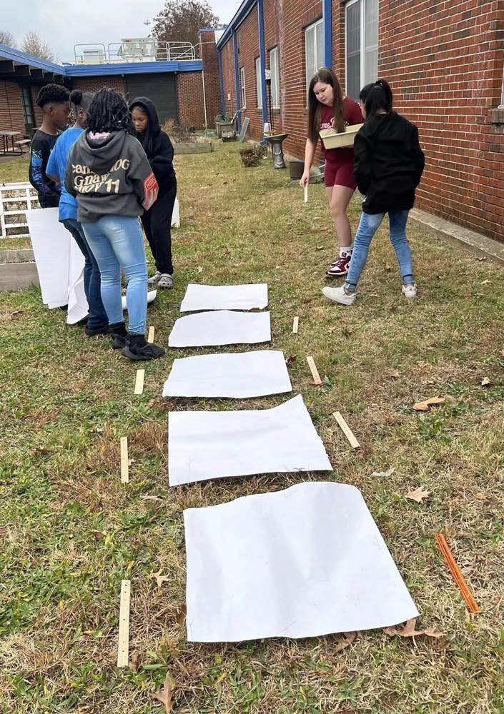 Students stand and work together, sketching and arranging materials as they create and design the GATE path at the Hawks Nest.