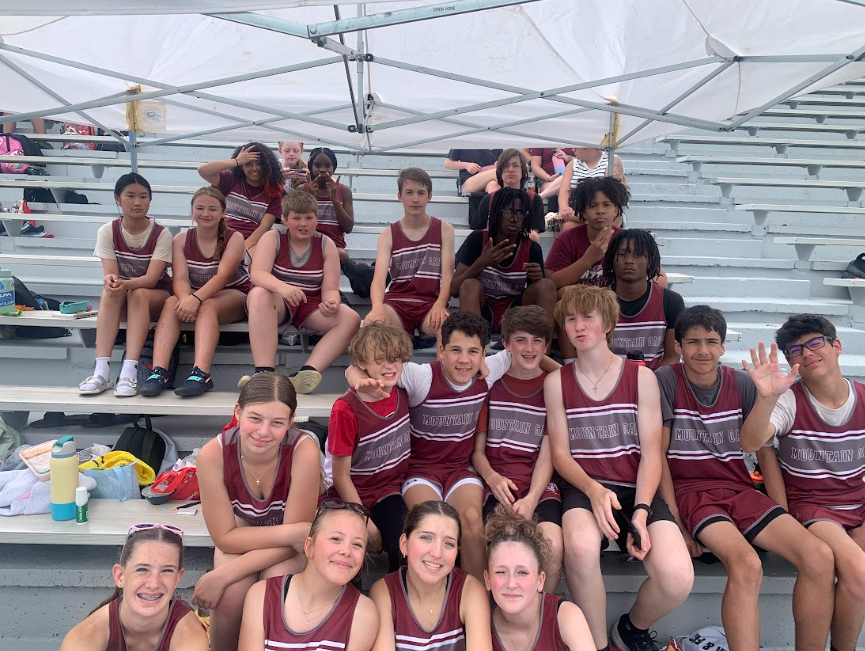 A group of track students sitting on the bleachers smiling for the camera