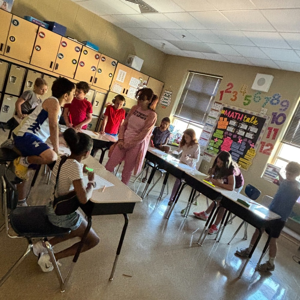 Math coach stands int he middle of a group of third grade students at their desks in a classroom.
