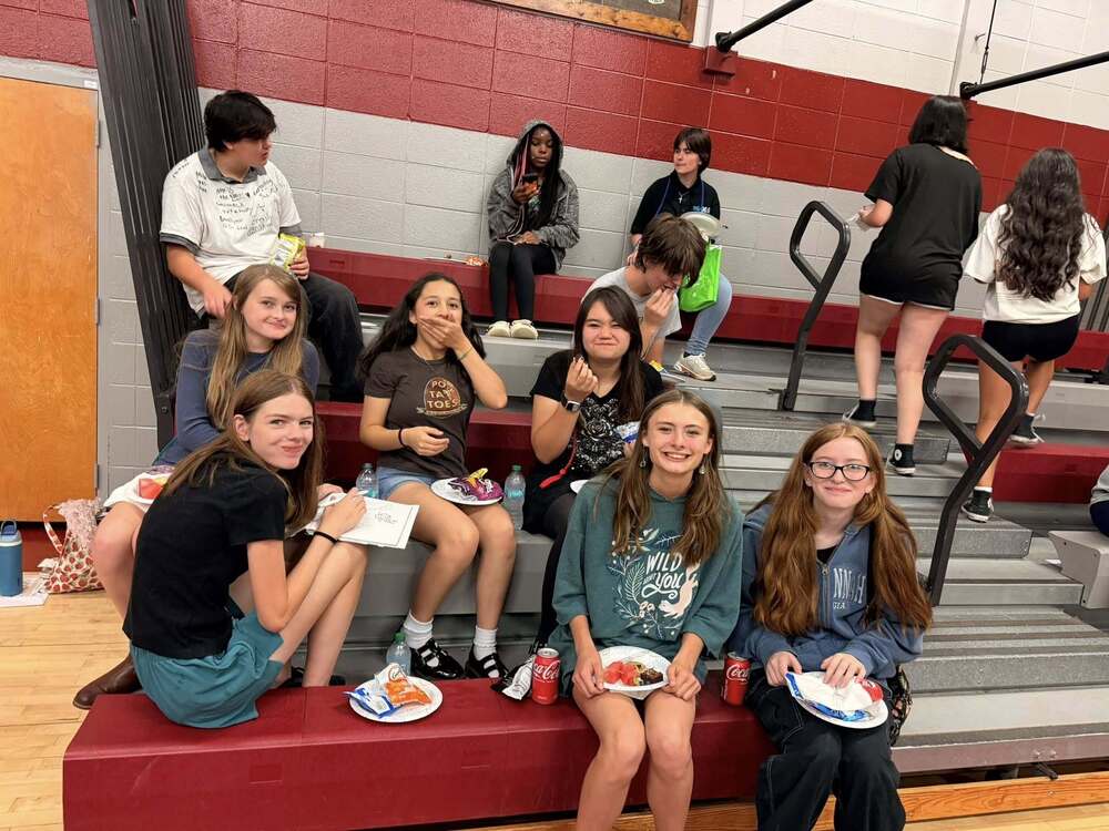 A group of students sitting on the bleachers enjoying pizza at their 8th grade picnic