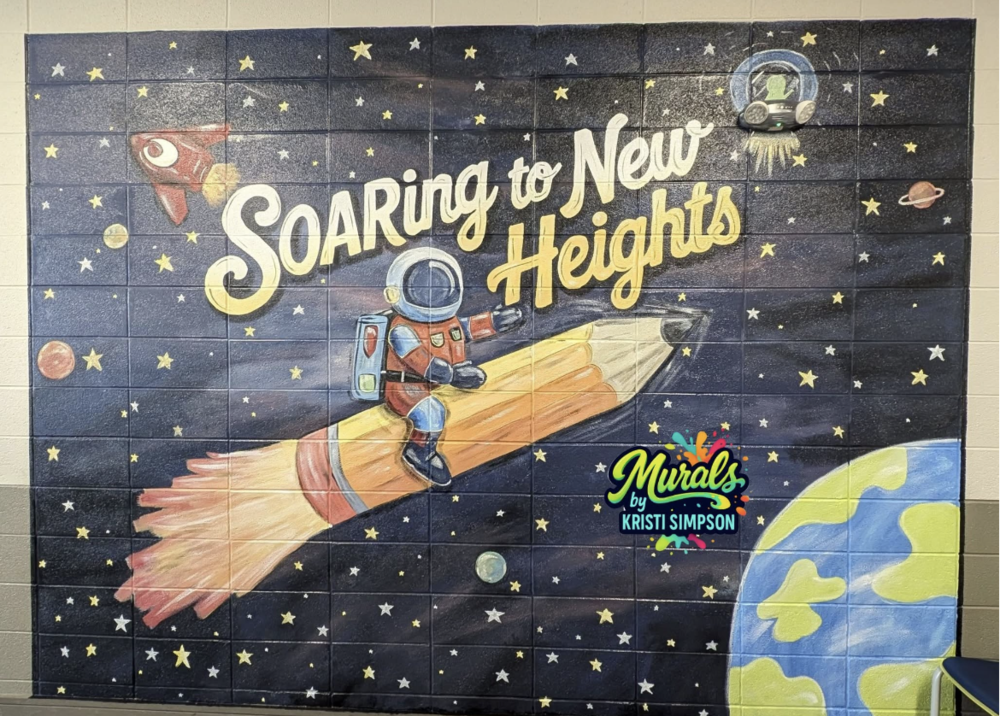 A mural on the wall of the school hallway featuring an astronaut riding a pencil through the plantes and stars