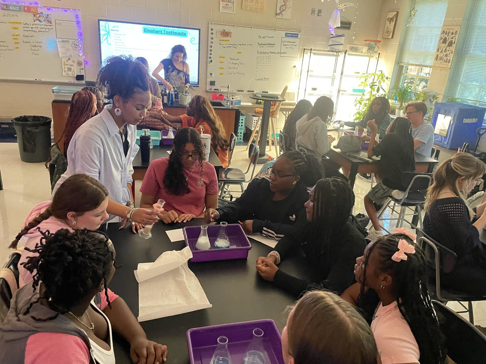 A group of studnets sit around a lab table doing an experiment.