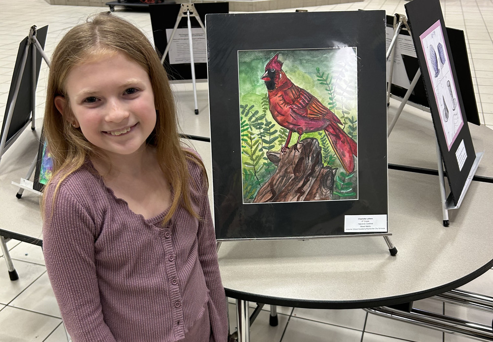 Female student stands next to artwork of a cardinal.
