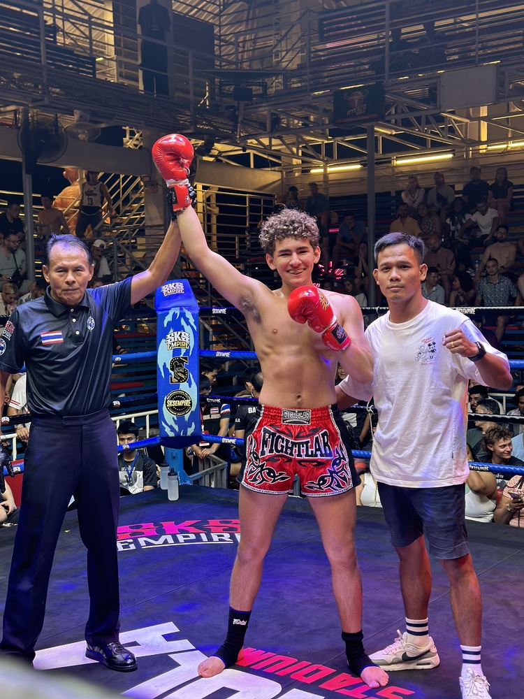 Young male student stands with two other men celebrating his win in his first professional fight.