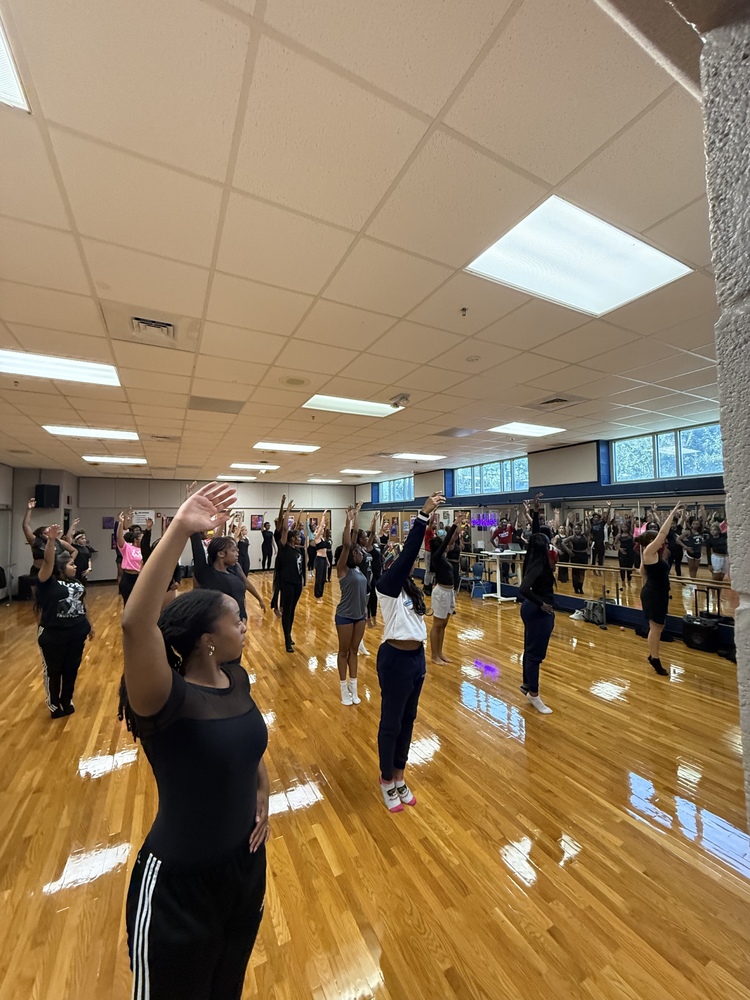 Lee High School Dance Magnet students participate in a workshop led by Troy University’s Department of Theatre and Dance in the Lee High dance studio. Students are positioned in front of mirrors, practicing choreography with arms raised in various dance poses on the polished studio floor.
